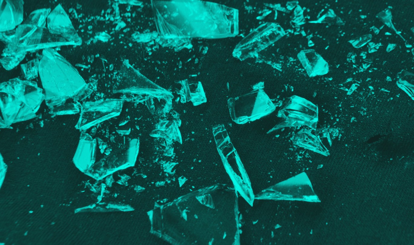 Scattered shards of glass on a dark surface, illuminated in teal tones.